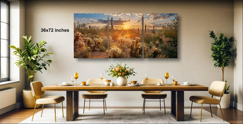 a large, framed desert landscape painting hanging on a wall above a wooden dining table set with wine glasses, plates, and a vase of flowers.