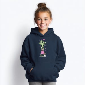 May include: A navy blue hoodie featuring a whimsical illustration of green aliens with pink hearts. The aliens are arranged in a vertical design, with a smaller alien figure wearing a pink dress. The hoodie has a front pocket and a hood.