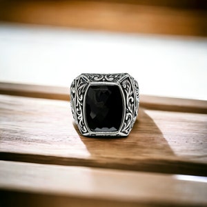 May include: A silver ring with an ornate design and a black gemstone in the center.