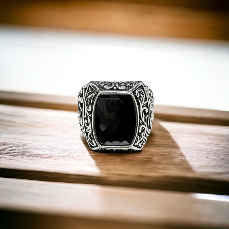 May include: A silver ring with an ornate design and a black gemstone in the center.
