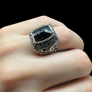 May include: A silver ring with an ornate design and a black gemstone in the center.