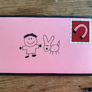 Könnte beinhalten: Eine rosa Karte mit schwarzem Rand. Auf der Vorderseite der Karte befindet sich eine Kinderzeichnung einer Person und eines Hundes. Oben rechts befindet sich ein roter Stempel mit einem schwarzen Hufeisen.