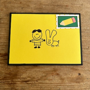 May include: A yellow card with a black border. A simple drawing of a person and a rabbit is on the card. A green and yellow pencil stamp is in the top right corner.