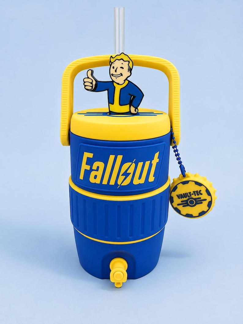 May include: A blue and yellow beverage cooler featuring the Fallout logo and a Vault Boy figure on the lid. The cooler has a yellow handle, a clear straw, and a blue beaded chain with a circular Vault-Tec tag attached to the side of the lid.