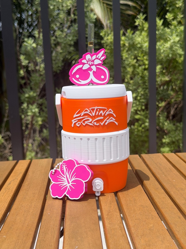 May include: An orange and white beverage cooler featuring the text "LATINA FOREVA" in white script. The cooler includes a clear straw with a pink floral topper and a separate pink hibiscus flower charm attached to the front near the white spigot.