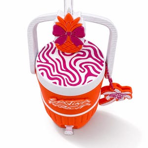 May include: An orange beverage cooler with a white handle and a white lid featuring a pink wavy pattern. The lid has a pineapple topper with a pink bow. A clear straw protrudes from the top. The cooler features the text "Living For It" and a palm tree charm.