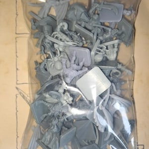 May include: A clear plastic resealable bag filled with a collection of unpainted grey miniature figures. The assortment includes various creatures and characters, such as a scorpion, a spider, and humanoid figures, each attached to a square base.