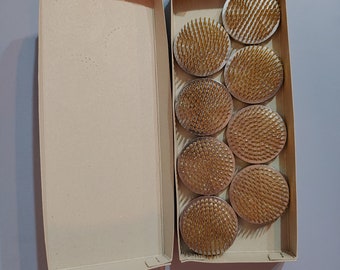 May include: A box of eight round floral foam bases with gold-colored pins. The bases are arranged in two rows of four in a cardboard box.