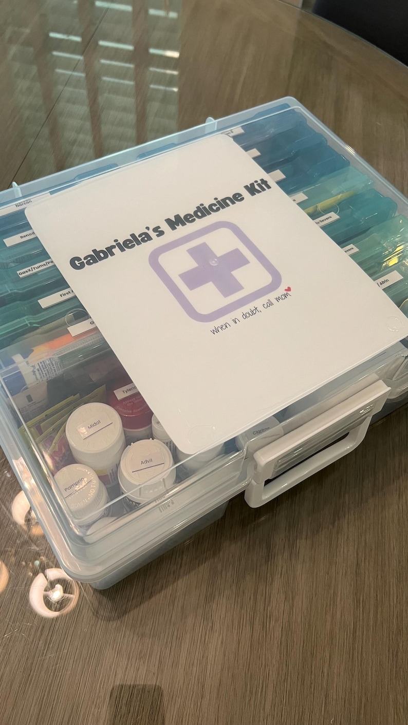 May include: A clear plastic medicine box with a white label that says "Gabriela's Medicine Kit" with a purple cross and the text "when in doubt, call mom". The box is filled with various medications and supplies.