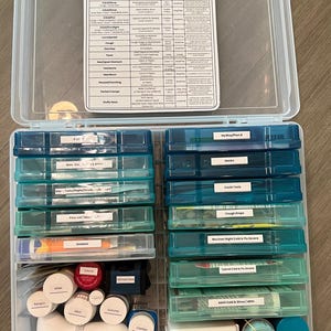 May include: A clear plastic storage box with a blue and white label that says "Gabriela's Medicine Kit". The box is filled with various medications and medical supplies, including first aid items, cough drops, cold and flu medicine, and batteries. The box is organized into compartments with labels for each item.