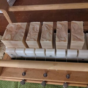 May include: Five bars of handmade soap in a wooden soap cutter. The soap is a light brown color with swirls of white.