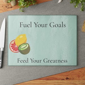 Könnte beinhalten: Ein rechteckiges Schneidebrett mit dem Text "Fuel Your Goals" und "Feed Your Greatness". Das Brett zeigt Illustrationen einer Grapefruit, Zitrone und Kiwi auf hellblauem Hintergrund.