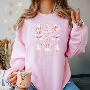 May include: Pink Christmas sweatshirt with a watercolour design featuring Santa, a Christmas tree, a reindeer, a fairy, and bows.