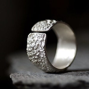 May include: A silver ring with a textured, hammered finish. The ring is open on one side and has a smooth, polished interior.