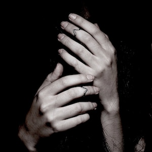 May include: Two silver rings with a V-shaped design on the fingers of a person's hands.