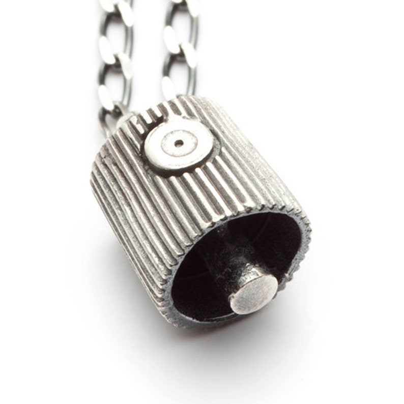 May include: Silver spray paint can cap pendant necklace. The cap has a textured, ribbed design and a small circular detail on the top.