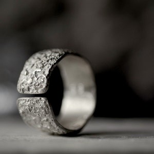 May include: A silver ring with a textured, rough surface. The ring has a gap in the band.