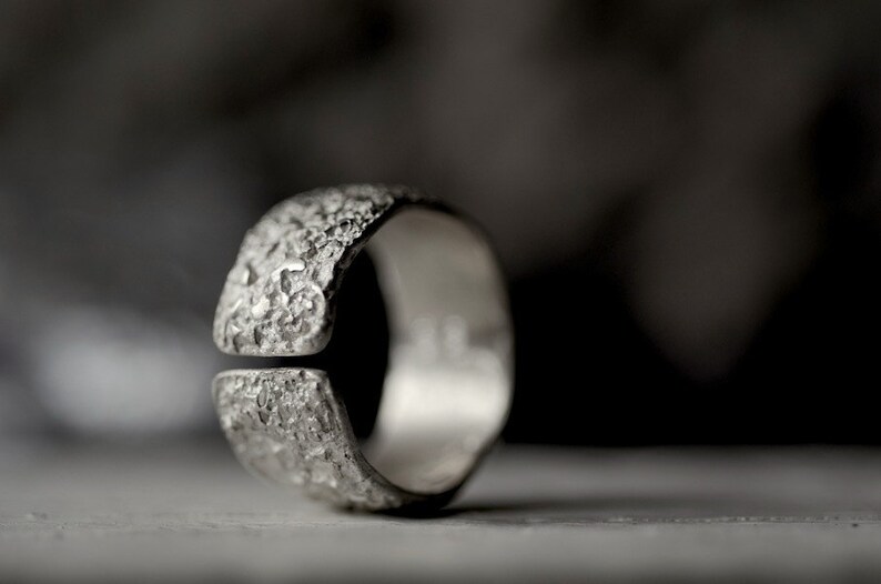 May include: A silver ring with a textured, rough surface. The ring has a gap in the band.