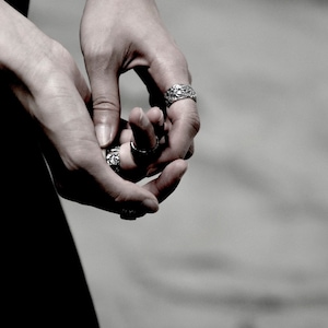 May include: Close-up of a person's hands wearing several silver rings with intricate designs.