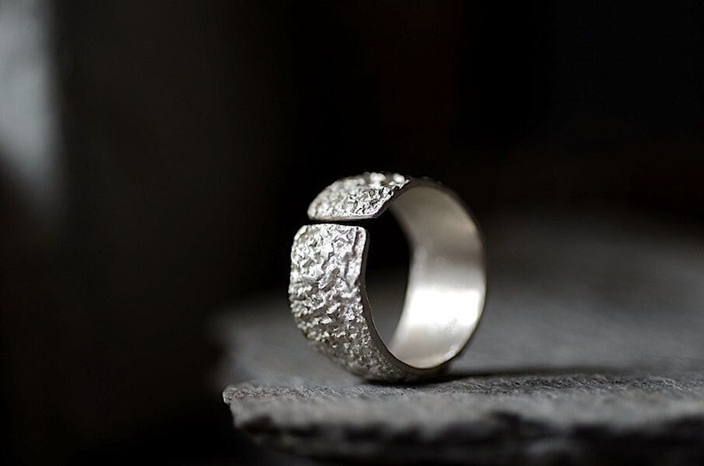 May include: A silver ring with a textured, hammered finish. The ring is open on one side and has a smooth, polished interior.