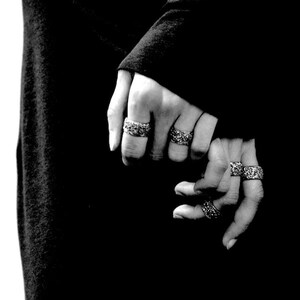 May include: Two hands wearing multiple silver rings. The rings are intricate and detailed.