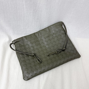 May include: An olive green rectangular clutch bag featuring a woven leather pattern across the entire front surface. The bag includes thin matching leather drawstrings that loop through the top edge and secure with a small, flat leather tab.