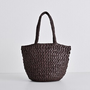 May include: A dark brown woven tote bag with two handles. The bag has a rounded shape and a textured surface. The handles are also woven and are attached to the top of the bag.