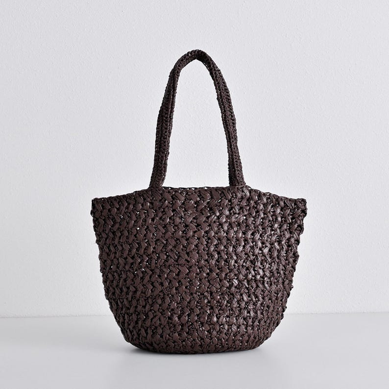 May include: A dark brown woven tote bag with two handles. The bag has a rounded shape and a textured surface. The handles are also woven and are attached to the top of the bag.