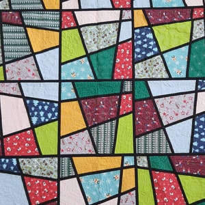 Könnte beinhalten: Ein farbenfroher Quilt mit einem Buntglas-Design. Der Quilt besteht aus verschiedenen Stoffen mit unterschiedlichen Mustern, darunter Weihnachtsbäume, Schneeflocken und Sterne. Der Quilt ist mit schwarzem Stoff gerahmt.