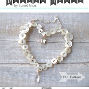 May include: A white button heart necklace with a crystal pendant. The necklace is on a wooden surface with the text "BUTTON HEART by Sweet Meas" and "PDF Pattern" on the image.