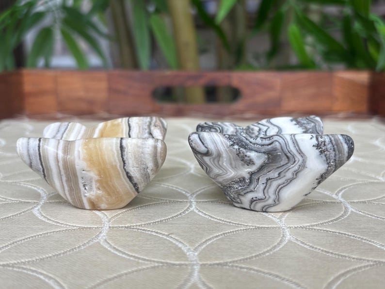 May include: Two decorative stone bowls with a unique shape. One bowl features a mix of beige, white, and brown tones, while the other has a black and white pattern. The bowls are placed on a patterned surface.