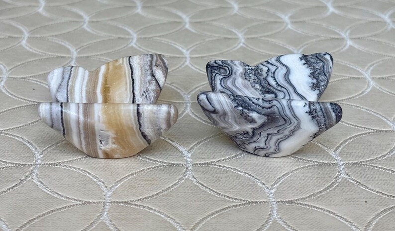 May include: Two pairs of heart-shaped stone bowls. One pair features tan, brown, and white striped patterns. The other pair has a black, gray, and white marbled design. The bowls are displayed on a neutral-toned surface.