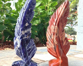 May include: Two carved stone feathers standing upright. One feather is deep blue with white marbled veins, and the other is a vibrant reddish-orange with darker streaks and light veining. Both pieces feature detailed etched lines mimicking a feather.