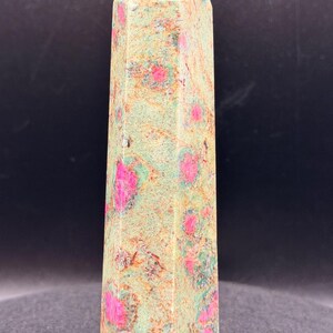 May include: A tall, faceted crystal obelisk. The stone features a mottled pattern of light green, tan, and vibrant pink spots. The obelisk has a pointed top and a rectangular base. This decorative item is suitable for home decor.