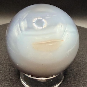 May include: A white ceramic mug with a black handle and the text "But First, Coffee" in a bold, black font. The mug is set against a neutral background, highlighting its simple design.