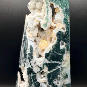 May include: A polished, rectangular gemstone with a mix of green, white, and yellow hues. The stone has a rough, textured surface with a geode-like cavity. The overall shape is a tall, obelisk-like form, perfect for display.