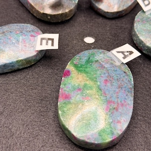 May include: A white ceramic mug with a black handle and the text "But First, Coffee" in a bold, black font. The mug is set against a blurred background, suggesting a cozy setting.