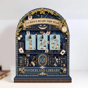 Op de afbeelding: Een grillige houten kalender in marineblauw, met de tekst "Curious Reads This Year" en "Wonderland Library". De kalender toont de cijfers "186" op lichtblauwe kaarten, met decoratieve speelkaarten en klokaccenten, met afmetingen in cm.