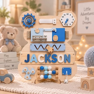 May include: A bear-shaped wooden activity board featuring the name JACKSON in blue letters. It includes a blue gear, a clock, a metal latch, a honey barrel icon, a sliding bear piece, a bead abacus, and a white bell on a string for sensory play.