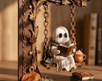 May include: A decorative wooden-style display featuring a ghost wearing a green scarf, reading a book on a swing suspended from a tree branch. The text "COZY READING SEASON" and "3-LAYER PRINTING" appear alongside pumpkins, books, and autumn leaves.