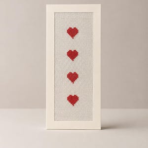 May include: A vertical rectangular card featuring a white perforated grid panel framed by a solid white border. Four red cross-stitched heart shapes are arranged in a single vertical column centered within the grid, creating a simple pattern.