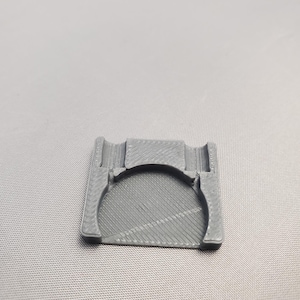 May include: A grey 3D printed plastic holder with a circular cutout.