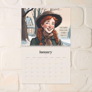 May include: A wall calendar featuring a smiling woman with red braids and a hat, set against a winter scene. The calendar page shows the month of January, with the quote "Life is worth living as long as there's a laugh in it."