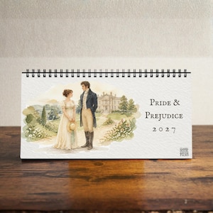 Puede incluir: Un calendario de escritorio con encuadernación en espiral que presenta una ilustración en acuarela de una pareja con vestimenta histórica frente a una gran finca. El texto dice Pride & Prejudice 2027, con un pequeño logotipo en la esquina.