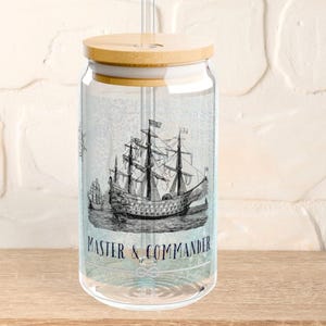 May include: A clear glass jar with a bamboo lid and a straw. The jar has a nautical theme with a black and white illustration of a ship and the text "Master & Commander".