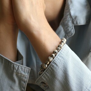 May include: A close-up of a person's wrist wearing a bracelet made of white and black speckled beads.