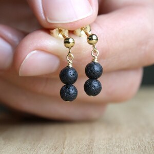 May include: A pair of gold earrings with two black lava rock beads on each earring.