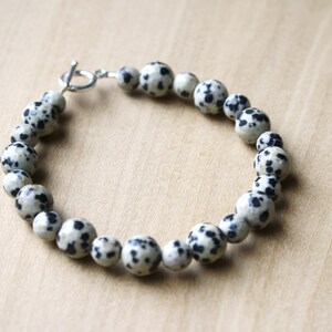 May include: A bracelet made of black and white dalmatian jasper beads with a silver toggle clasp.