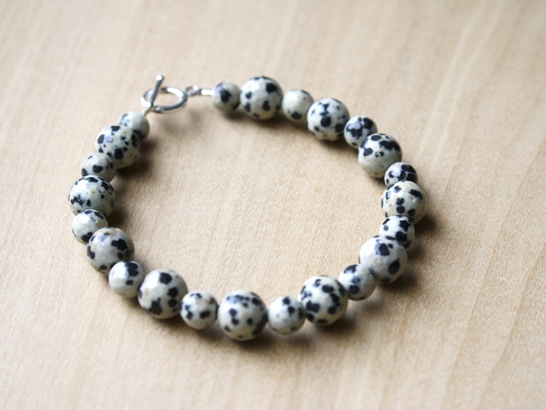 May include: A bracelet made of black and white dalmatian jasper beads with a silver toggle clasp.