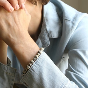 May include: A person wearing a light blue denim shirt with a bracelet made of white and black speckled beads.